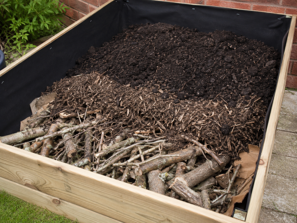 A deep raised bed part-filled with a bulky organic base layer of woody prunings before the topsoil and compost mix
